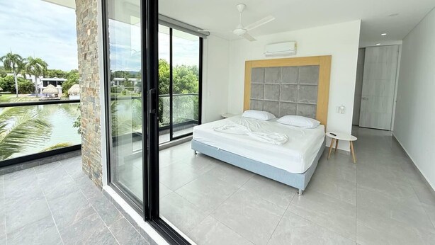 A modern bedroom with a large bed, a glass door leading to a balcony, and a view of greenery.