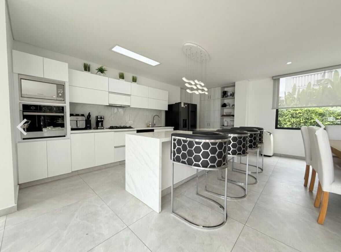 A modern kitchen with white cabinets, a central island, and bar stools.