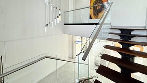 A modern interior with a glass railing, a staircase with wooden steps, and a painting on the wall.