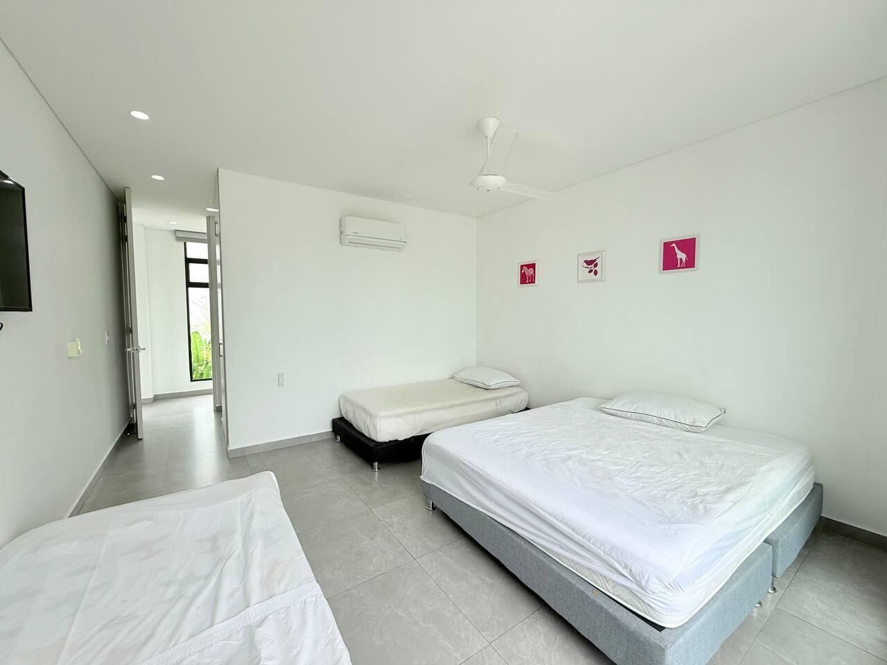 A modern hotel room with a large bed, a smaller bed, and a desk. There is a ceiling fan and an air conditioning unit.