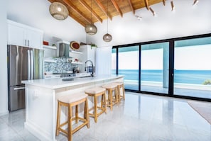 A modern kitchen with a large island, bar stools, and a view of the ocean.