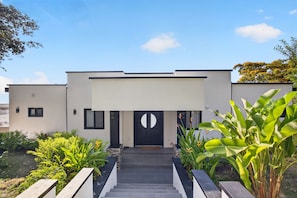 A modern building with a black door, a staircase leading to the entrance, and surrounding greenery.