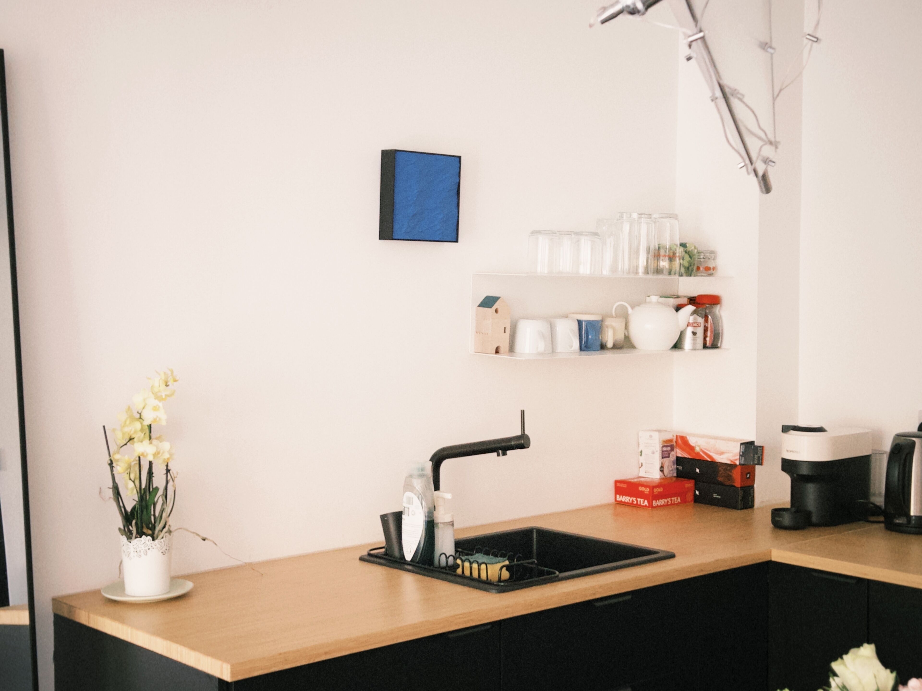 A kitchen with a wooden countertop, a sink, a coffee machine, and a shelf with kitchenware.