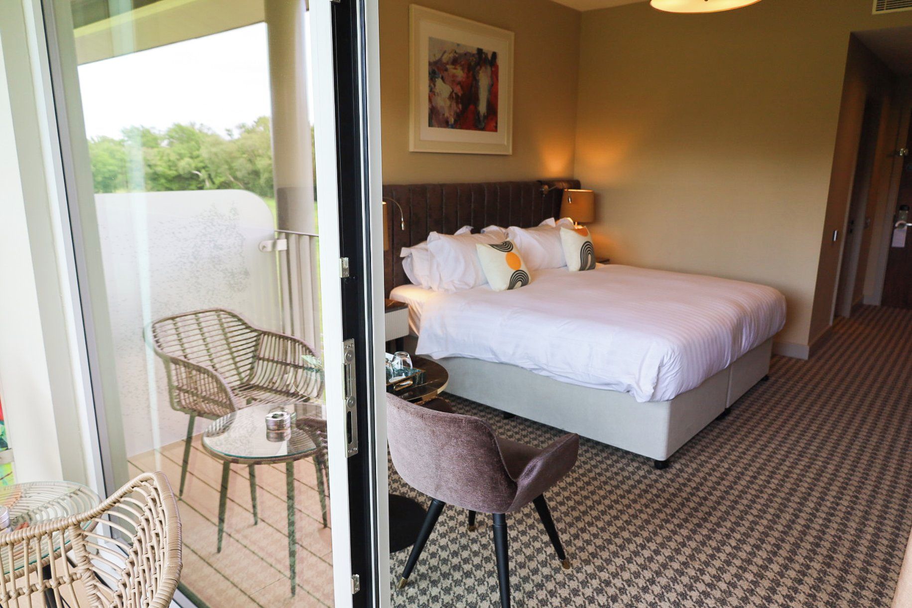 A hotel room with a bed, a chair, a table, and a painting on the wall.