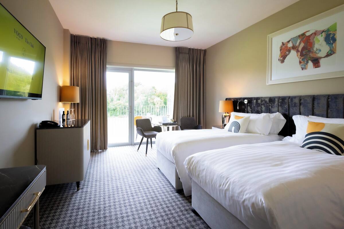 Een hotelkamer met twee bedden, een bureau, een stoel, een televisie en een groot raam.