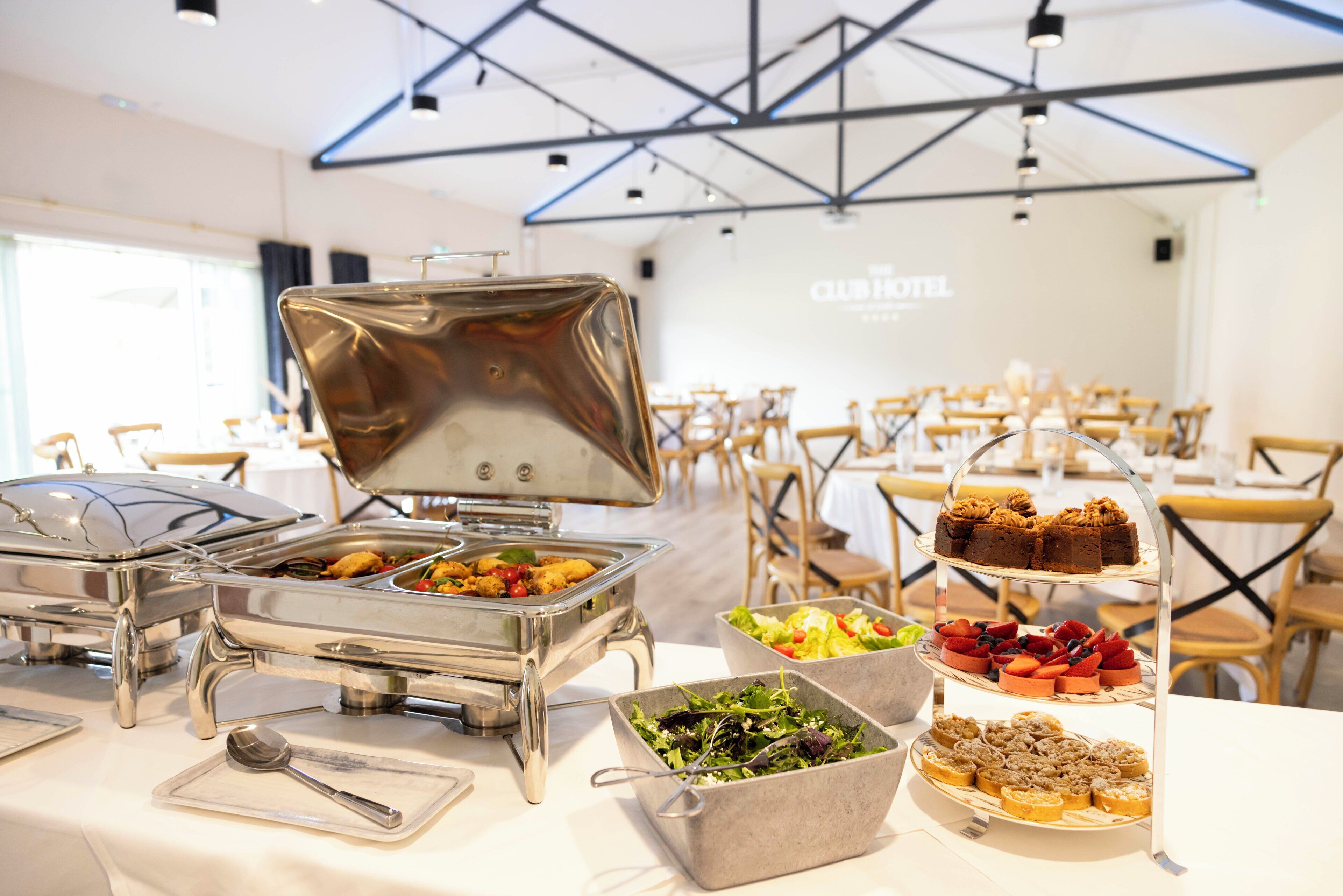 Disposición de bufé con diferentes opciones de comida y un soporte de postres de tres niveles en un comedor de hotel.