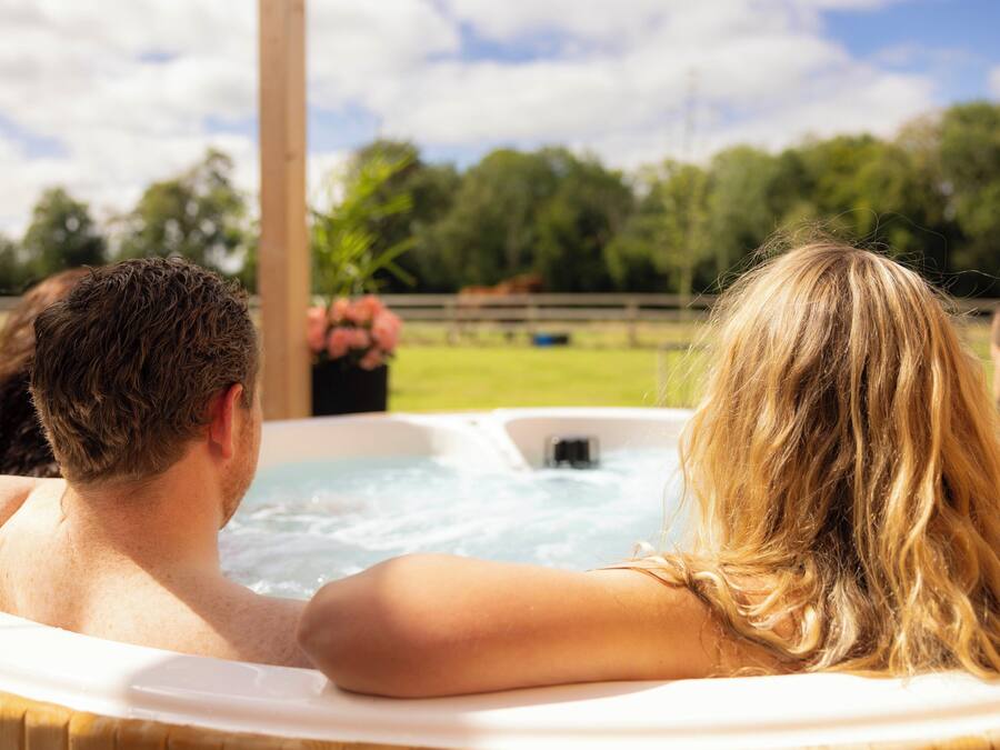 Un jacuzzi con dos personas, rodeado de césped y árboles.