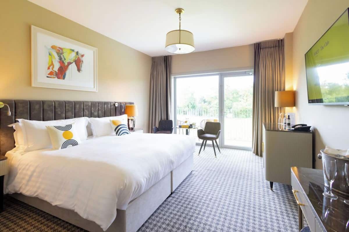 Hotelkamer met een groot bed, een bureau met een lamp, een stoel en uitzicht op de omgeving.