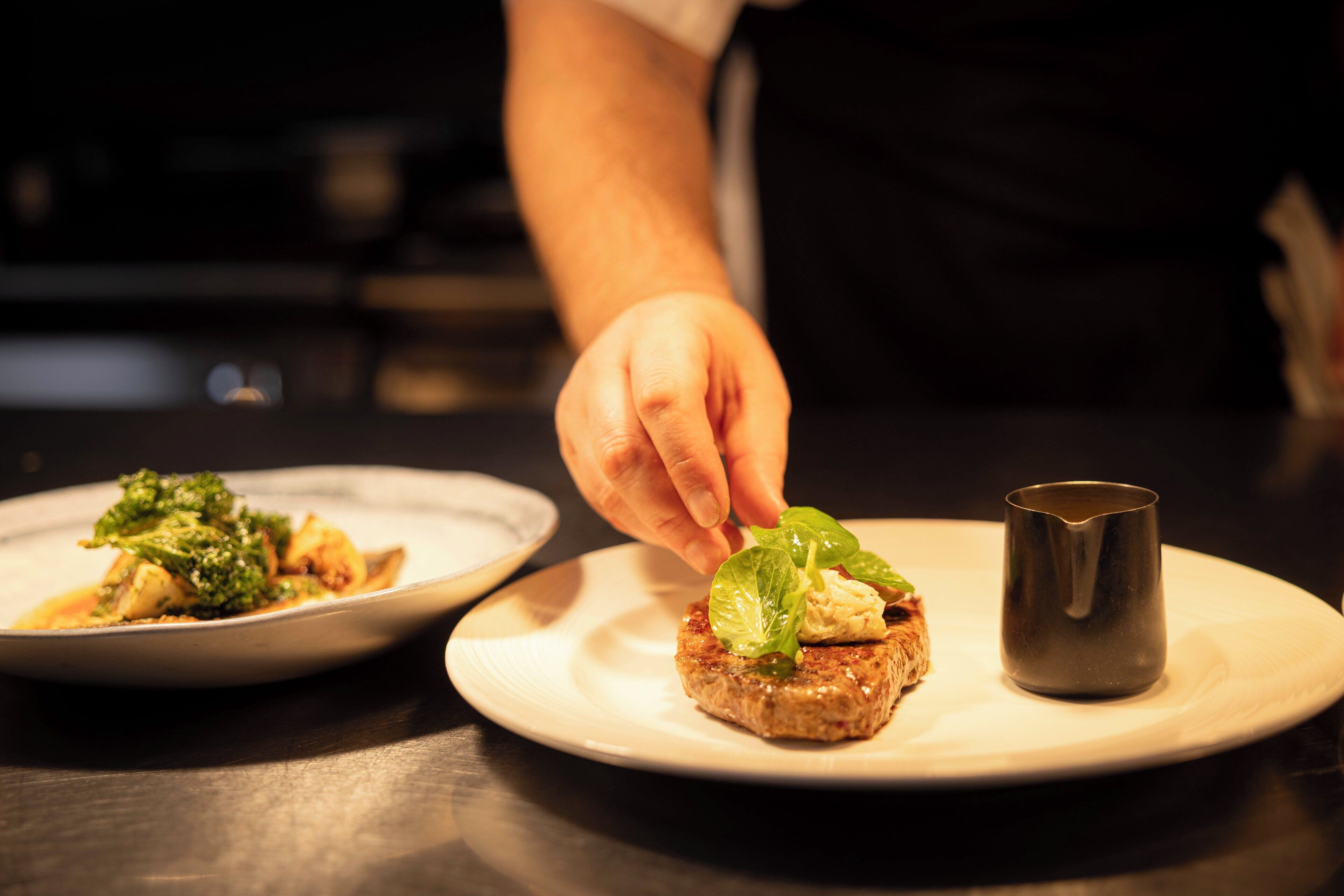 A chef placing a leaf on a food item on a plate.
