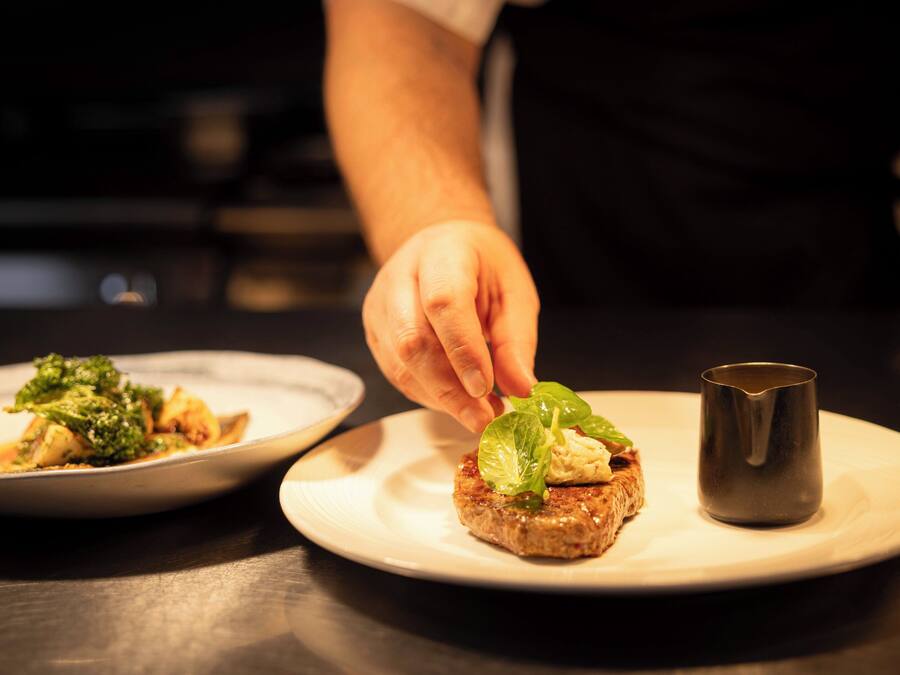 A chef placing a leaf on a food item on a plate.
