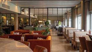 Ein modernes Restaurant mit Sitzboxen und Tischen, großen Fenstern und Zimmerpflanzen.