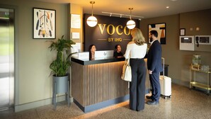 Ein Empfangsschalter mit einem Schild mit der Aufschrift 'Voco by IHG' und einer Zimmerpflanze daneben.
