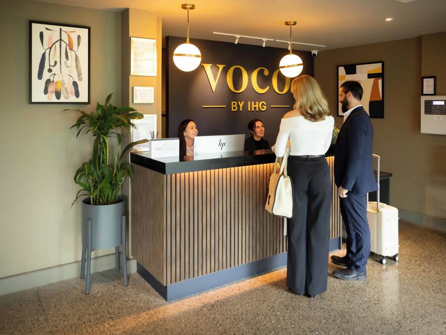 A reception desk with a sign reading "Voco by IHG" and a potted plant beside it.