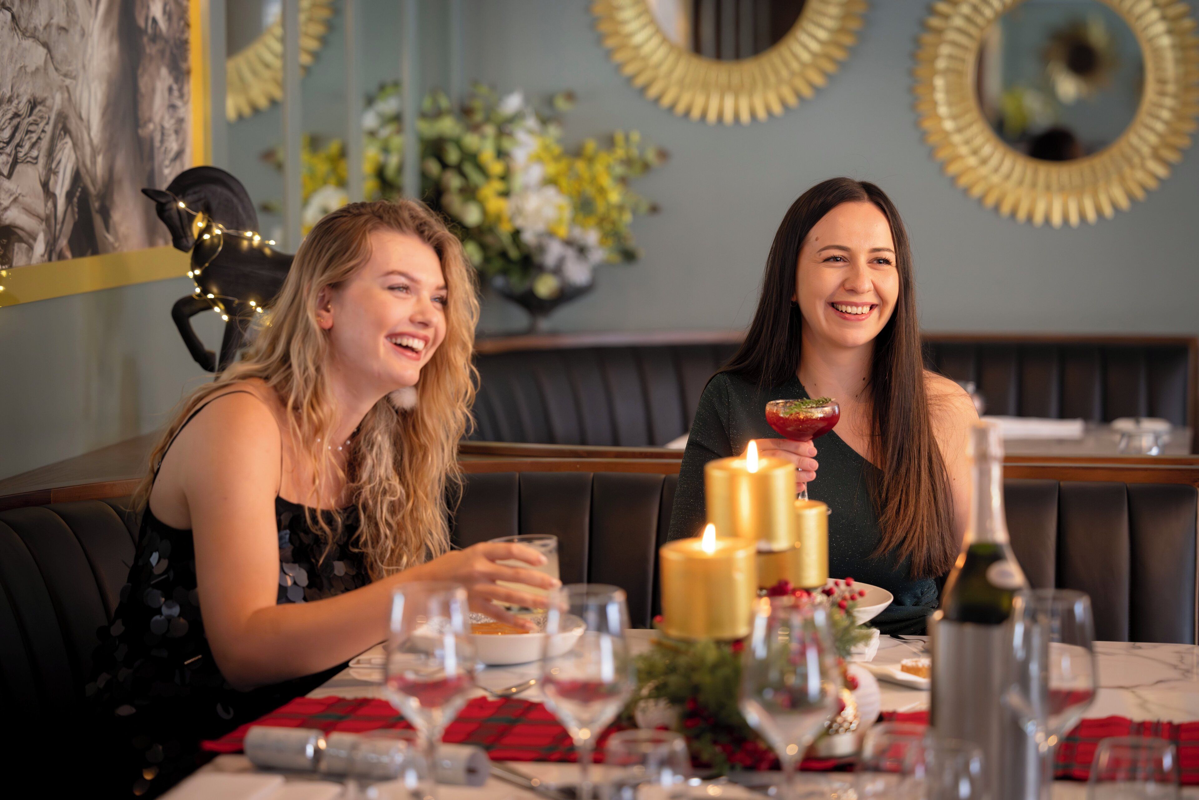 Twee personen zitten aan een tafel met kaarsen, een fles en een schaal eten.