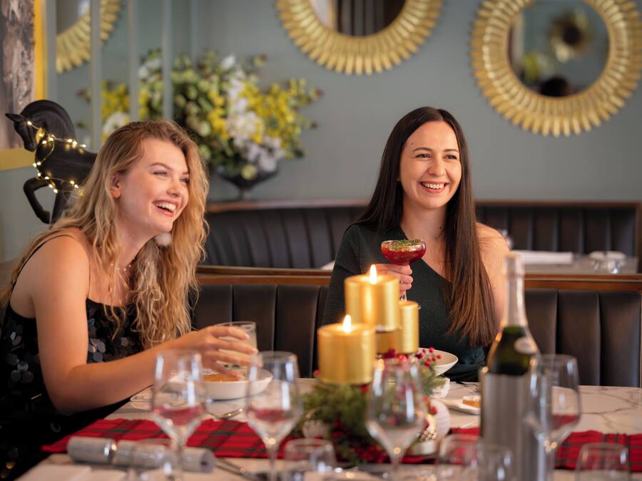Twee personen zitten aan een tafel met kaarsen, een fles en een schaal eten.