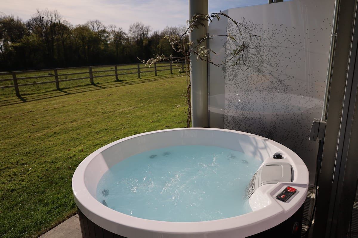 Een kuip met warm water en bedieningspaneel, omgeven door gazon en een houten omheining.