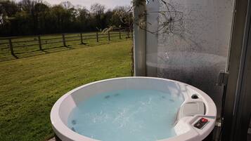 Un jacuzzi con panel de control, rodeado de césped y una valla de madera.