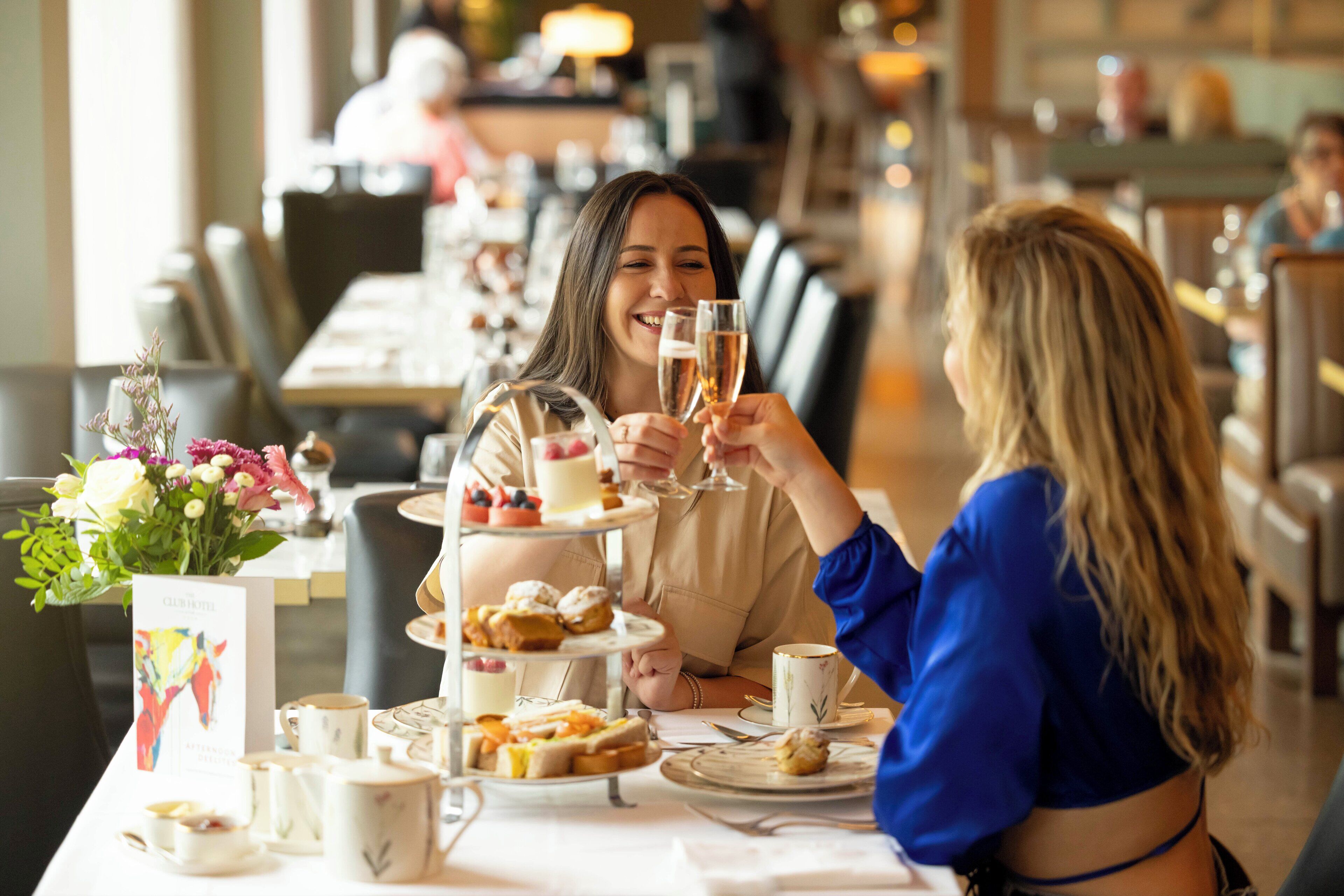 Un comedor con una mesa dispuesta para dos personas, que incluye un frutero escalonado, un centro de mesa floral y una vajilla de té.