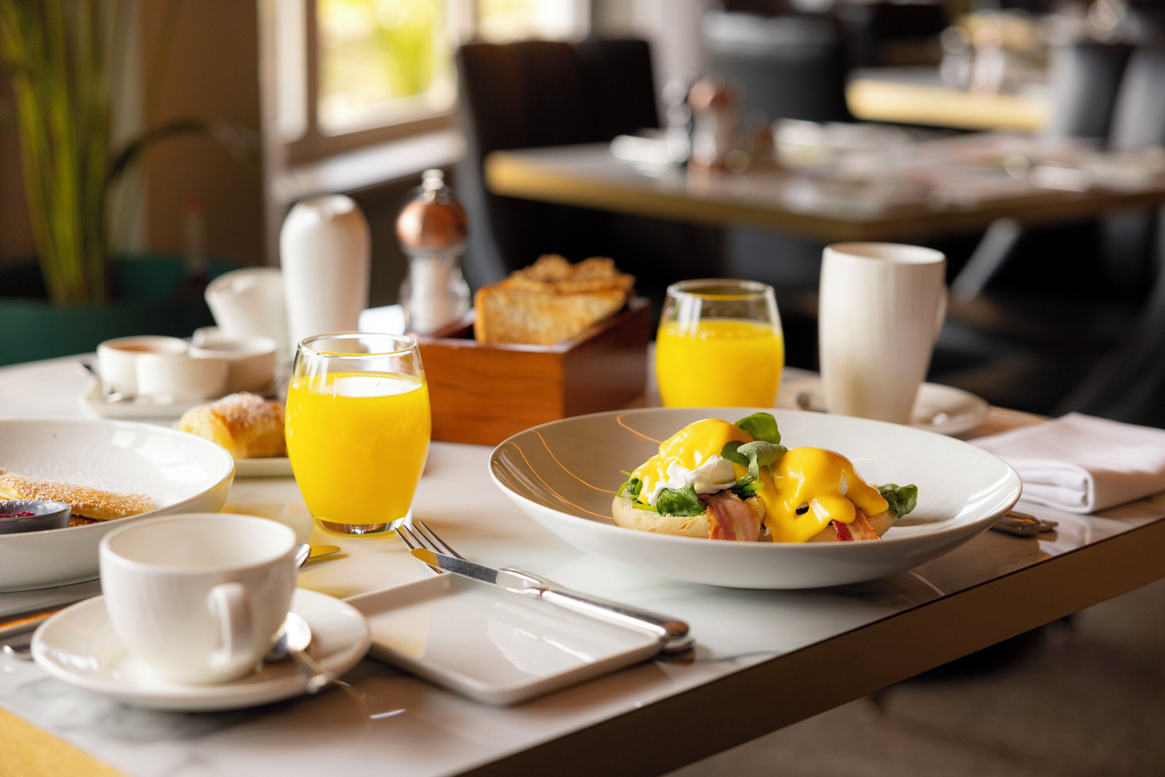 A breakfast setting with a plate of eggs benedict, a glass of orange juice, and a cup of coffee on a table.