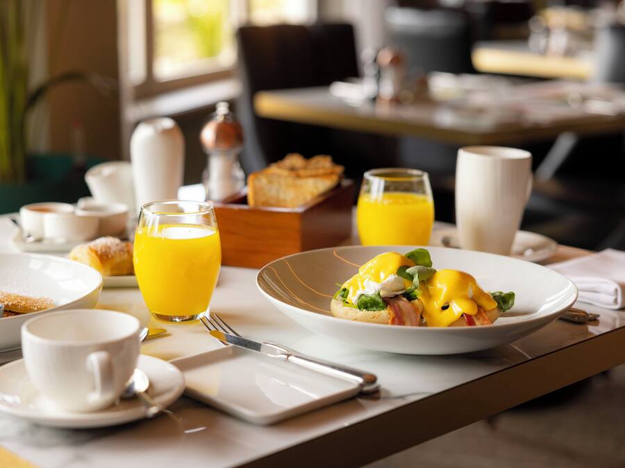 A breakfast setting with a plate of eggs benedict, a glass of orange juice, and a cup of coffee on a table.