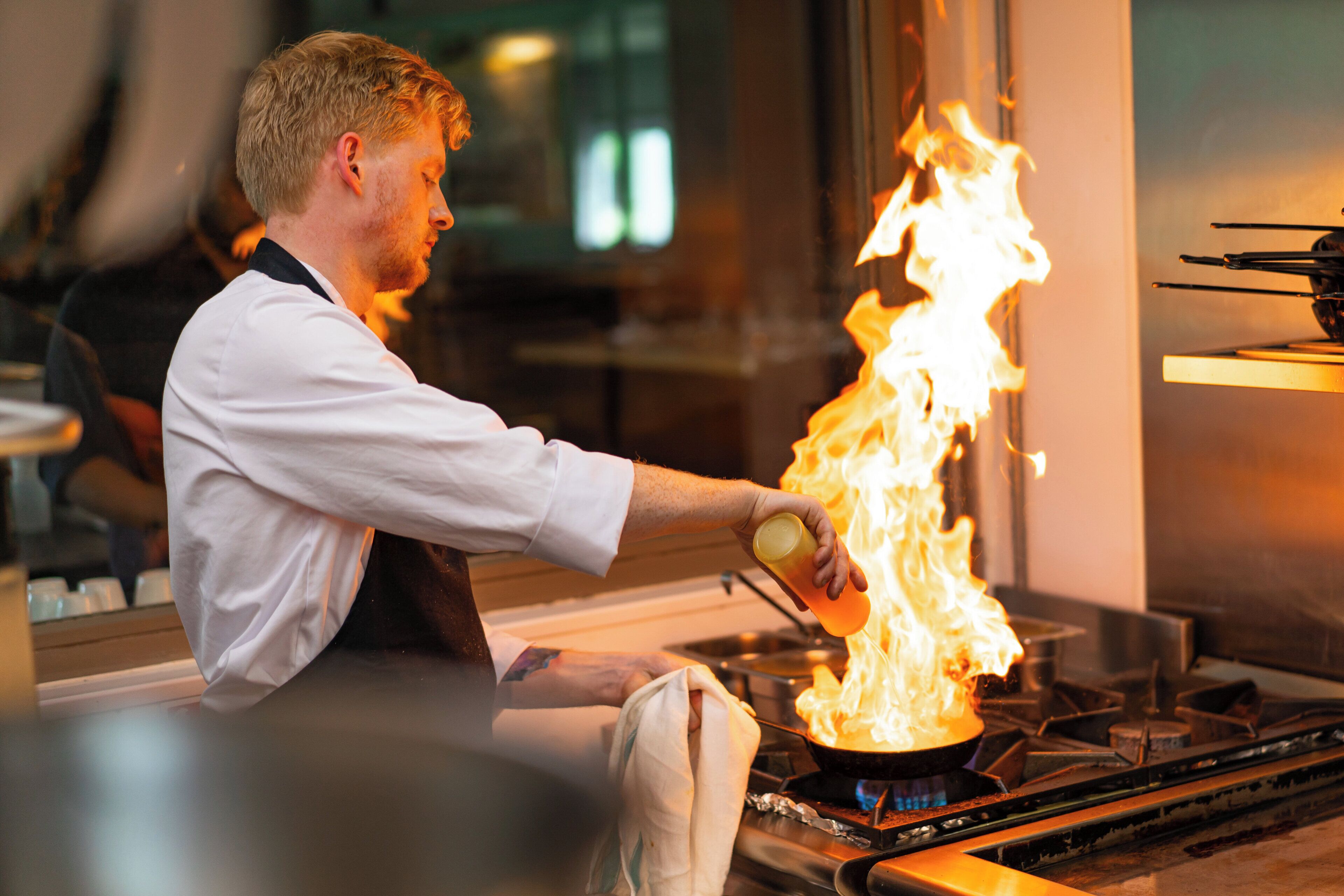A person pouring a liquid onto a stove, causing a flame.