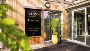 Ein Holzgebäude mit einem Schild für „Voco by IHG The Club“, das eine Rezeption, eine Bar und ein Restaurant anzeigt.