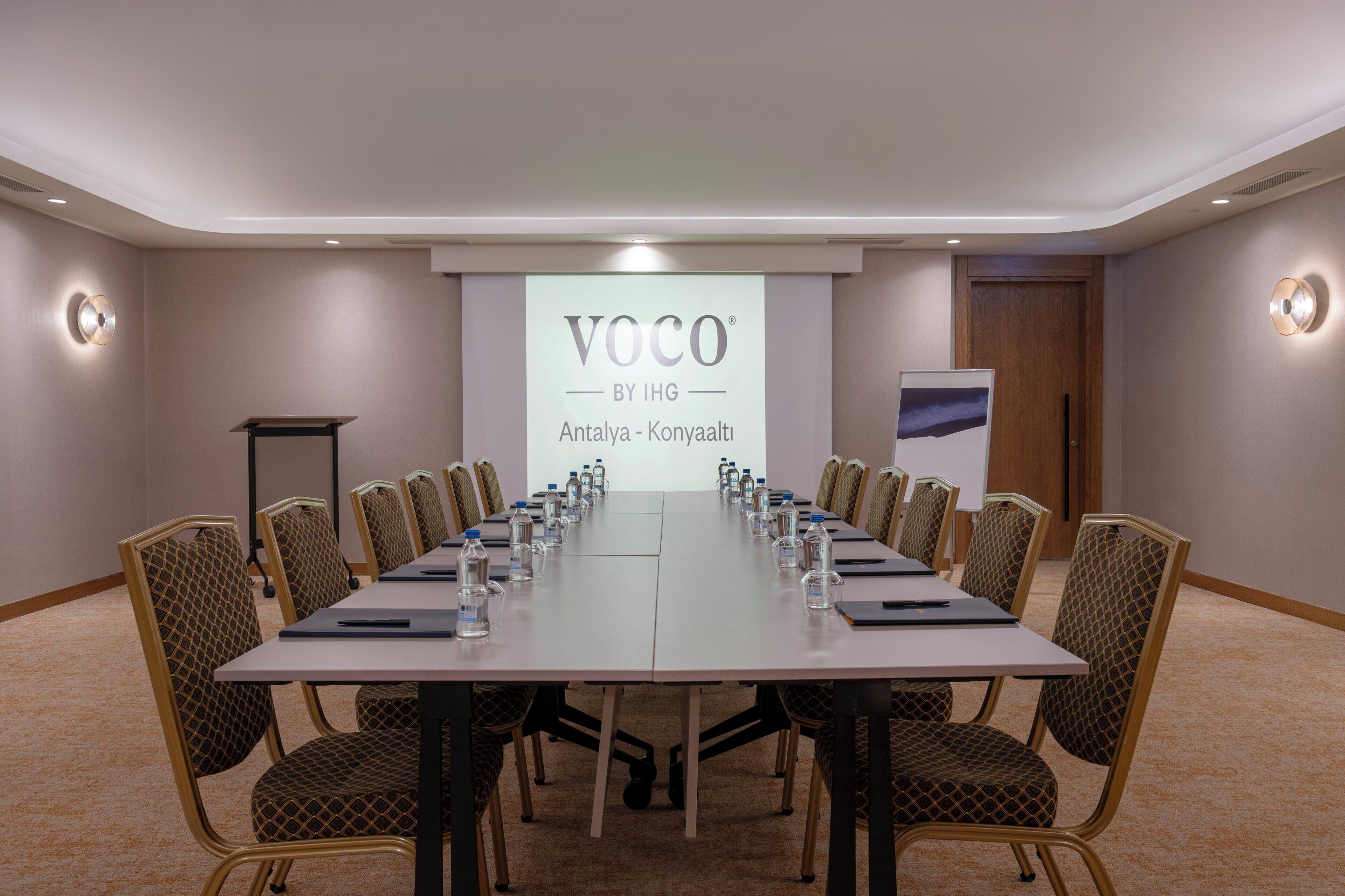Een vergaderzaal met een lange tafel, stoelen, waterflesjes en een presentatiescherm.