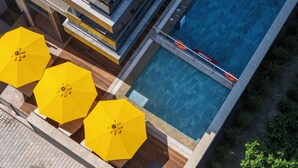 A rooftop pool area with three yellow umbrellas, a lifeguard stand, and a view of the surrounding buildings.