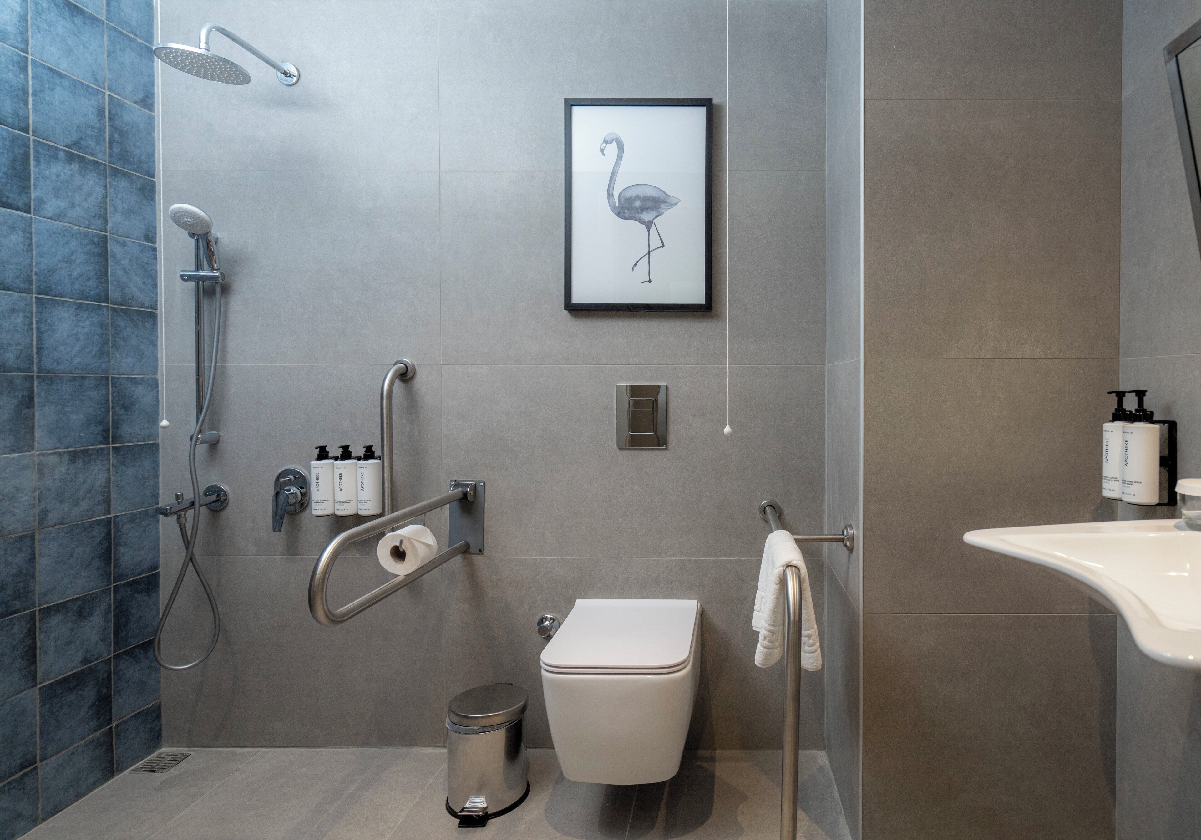 A modern bathroom with a shower, toilet, and sink, featuring a framed wall art of a flamingo.