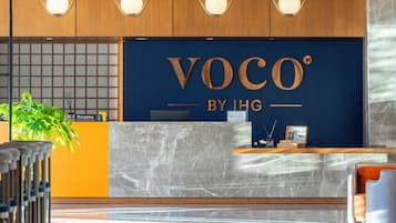 Una reception con una insegna che recita 'Voco by IHG' e un'area accoglienza con una pianta e un quadro incorniciato.