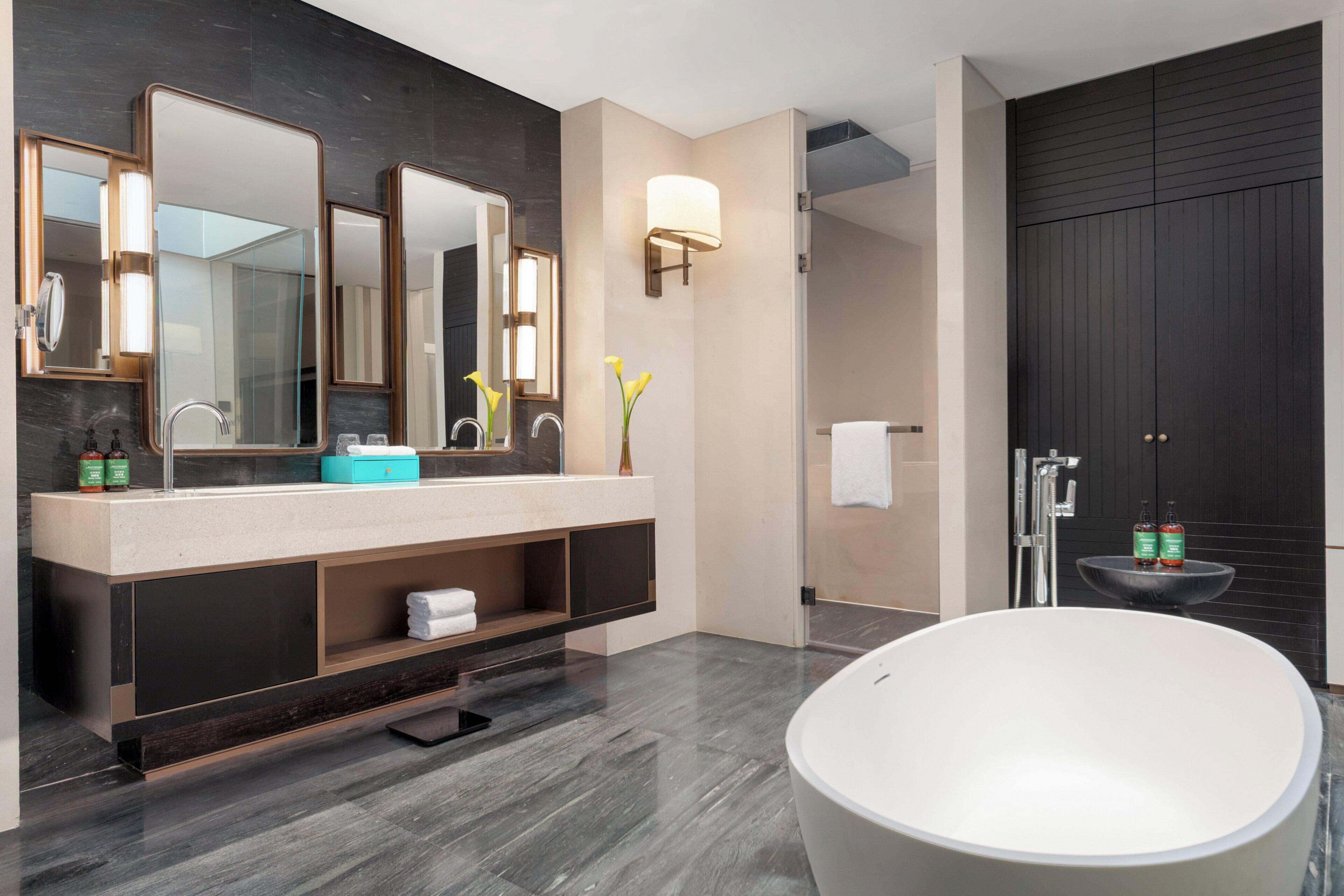 A modern bathroom with a freestanding bathtub, a large vanity with mirrors, and a separate sink area.