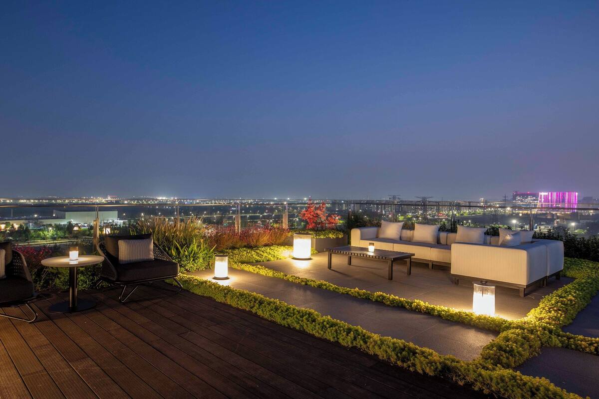 Eine Dachterrasse mit Außenmöbeln, Blick auf die Stadtlandschaft und beleuchteten Pflanzen.