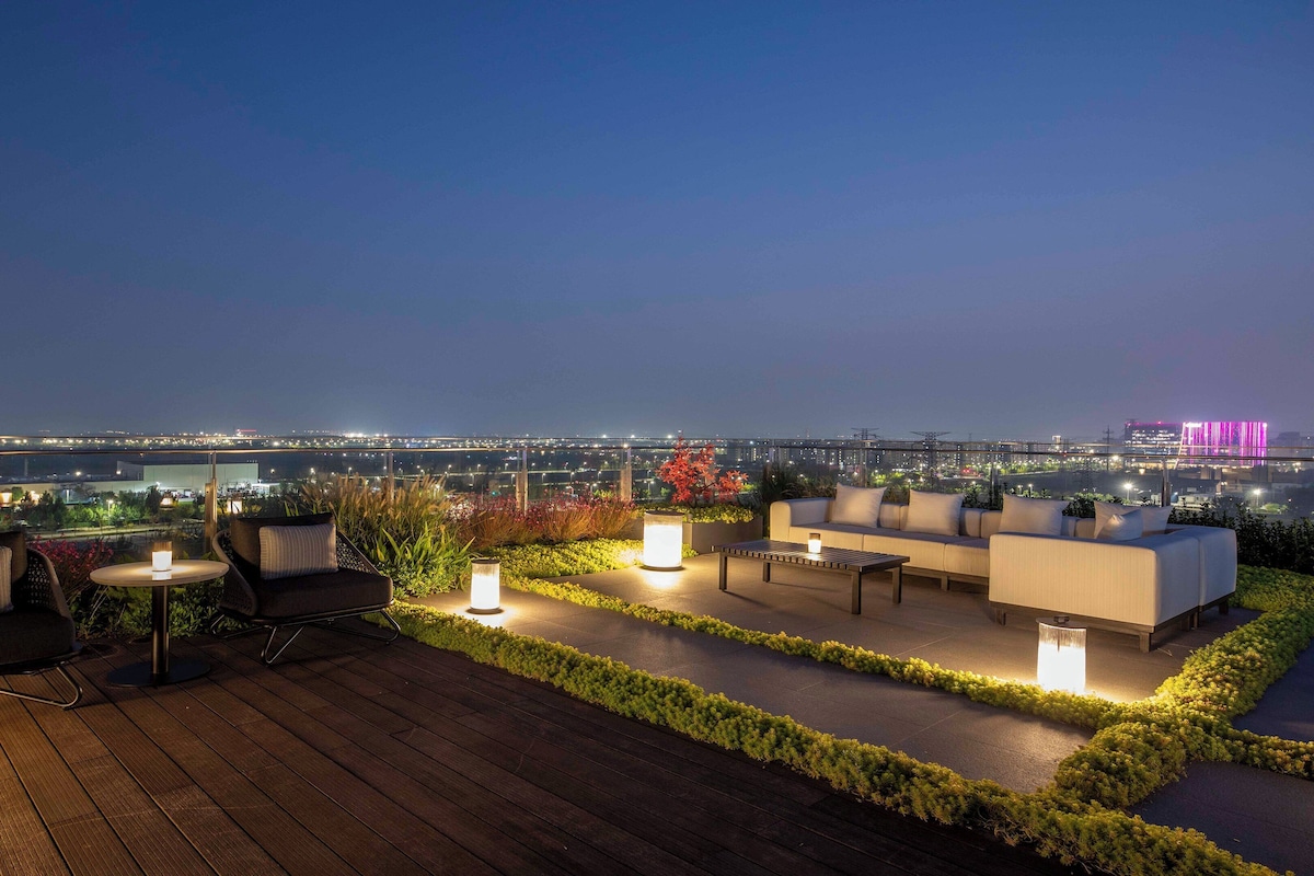 Eine Dachterrasse mit Außenmöbeln, Blick auf die Stadtlandschaft und beleuchteten Pflanzen.