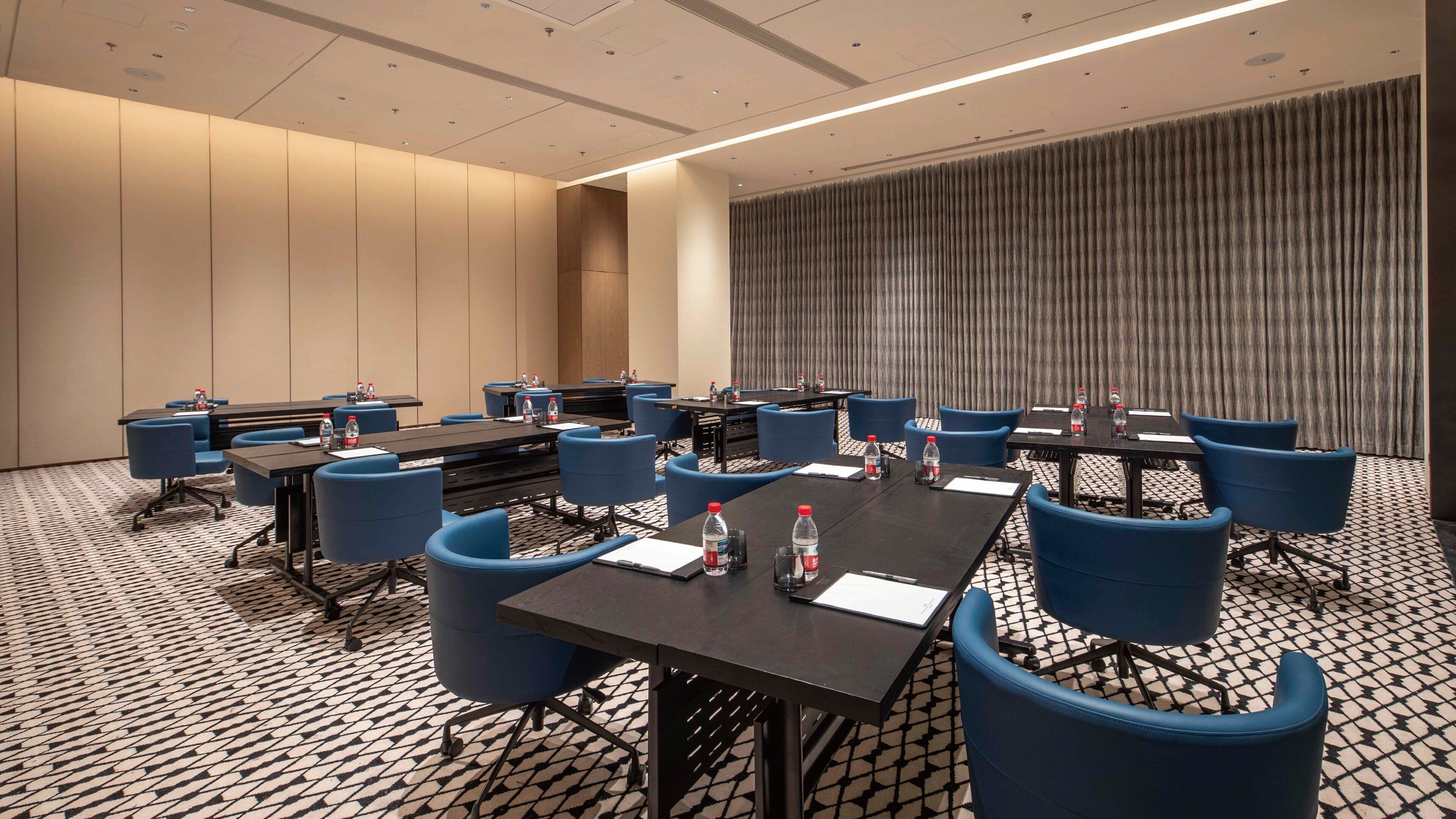 A conference room with multiple tables and blue chairs, equipped with water bottles and nameplates.