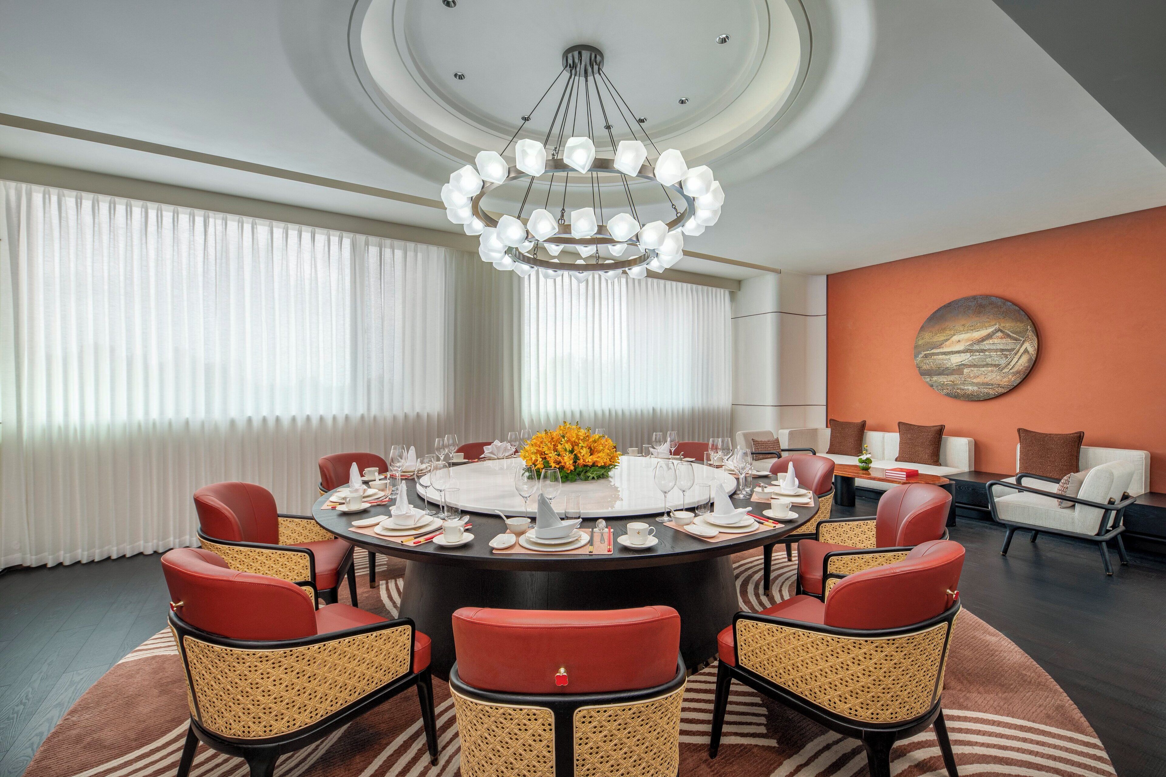 A round dining table with red chairs, a chandelier, and a vase of flowers.