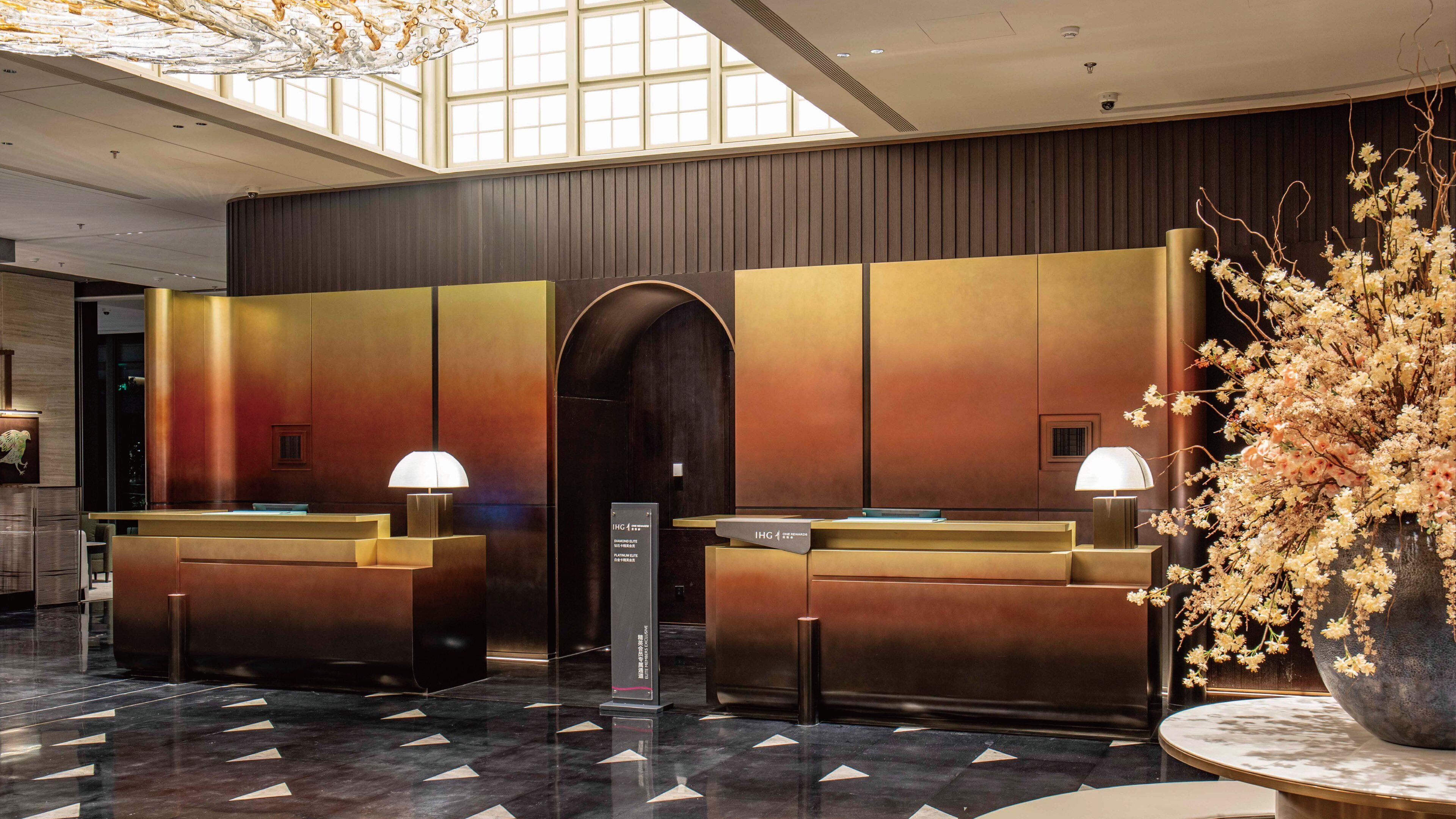 A reception area with a modern design, featuring a reception desk, a large vase with flowers, and a patterned floor.
