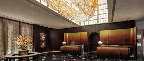 A modern hotel lobby with a reception desk, a decorative ceiling installation, and a large window providing natural light.