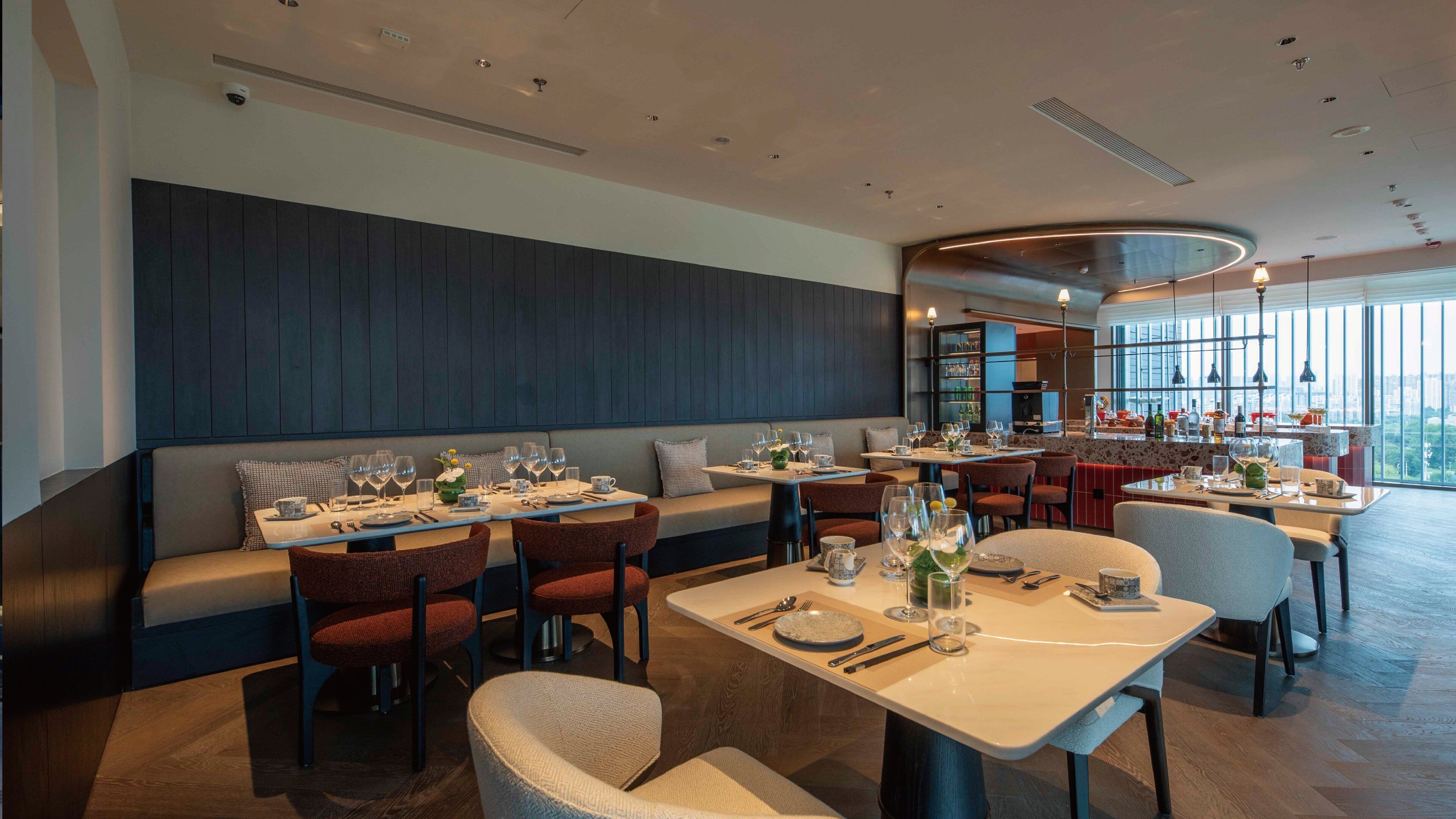 Ein modernes Restaurant mit hohen Tischen, Sitzbänken, einer Bar und großen Fenstern mit Blick auf die Stadt.