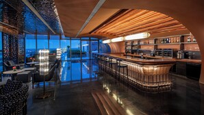 A modern bar area with a reflective floor, a curved bar counter, and a view of the cityscape through large windows. - Crowne Plaza Beijing Tongzhou by IHG (Tongzhou)