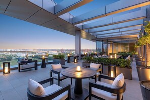 Une terrasse sur le toit, avec des espaces de détente en plein air, des plantes en pot et une vue sur le paysage urbain.