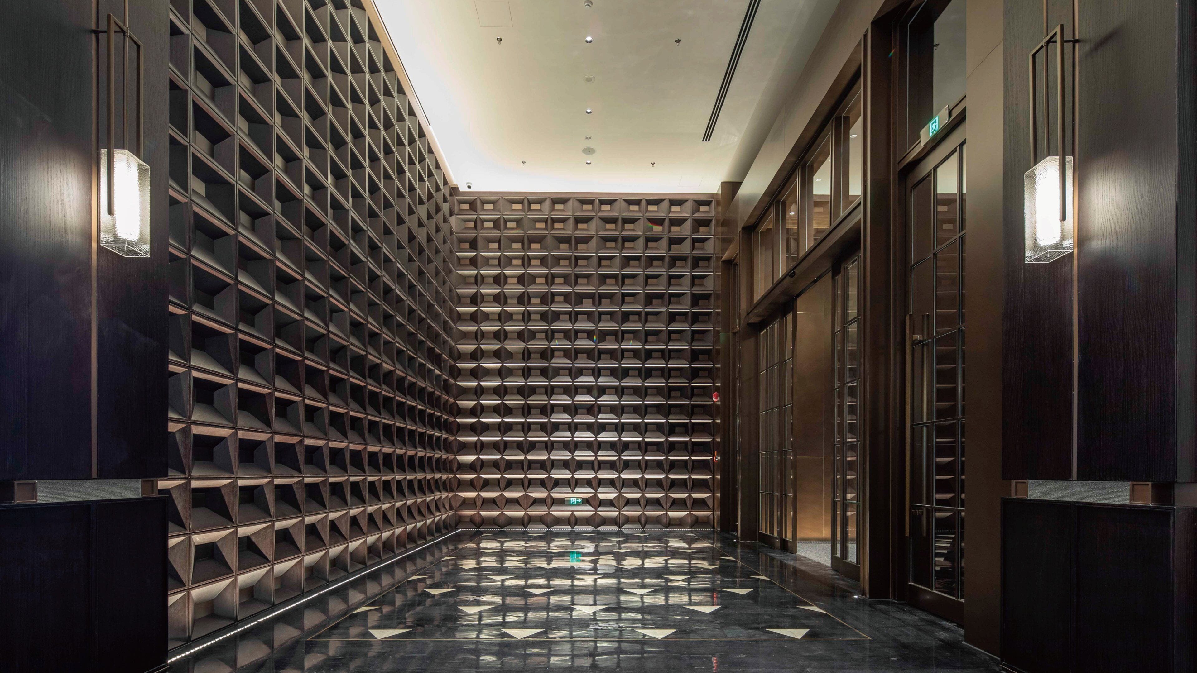 A hallway with a patterned wall and a polished floor, leading to a door.
