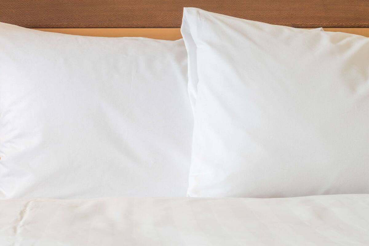 Ein Bett mit weißer Bettwäsche und Kissen vor einem Holzkopfschild.