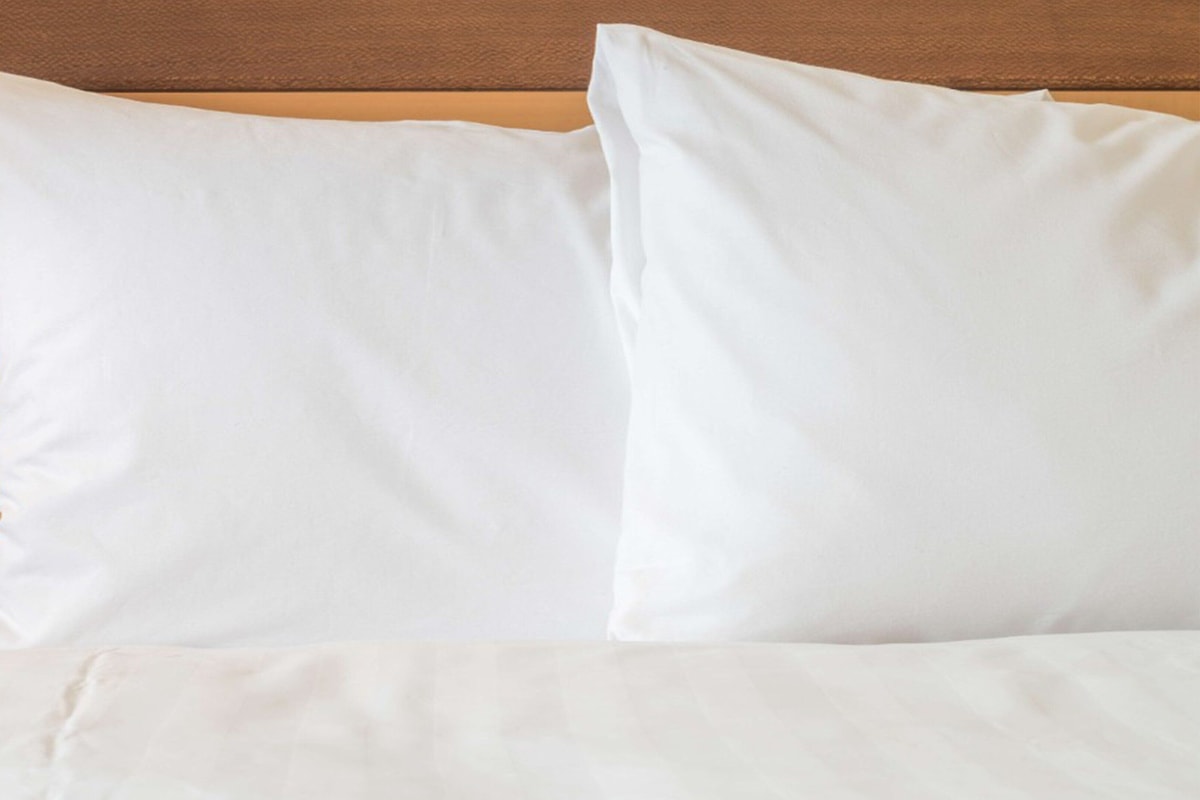 Ein Bett mit weißer Bettwäsche und Kissen vor einem Holzkopfschild.