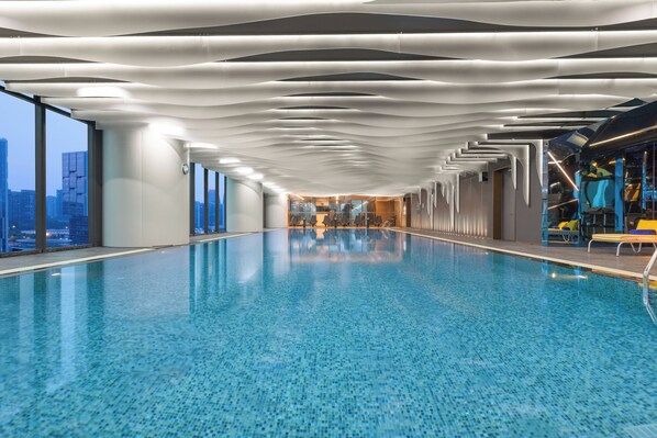 Une piscine intérieure moderne avec vue sur la ville, un design épuré au niveau du plafond et un mur en verre sur un côté.