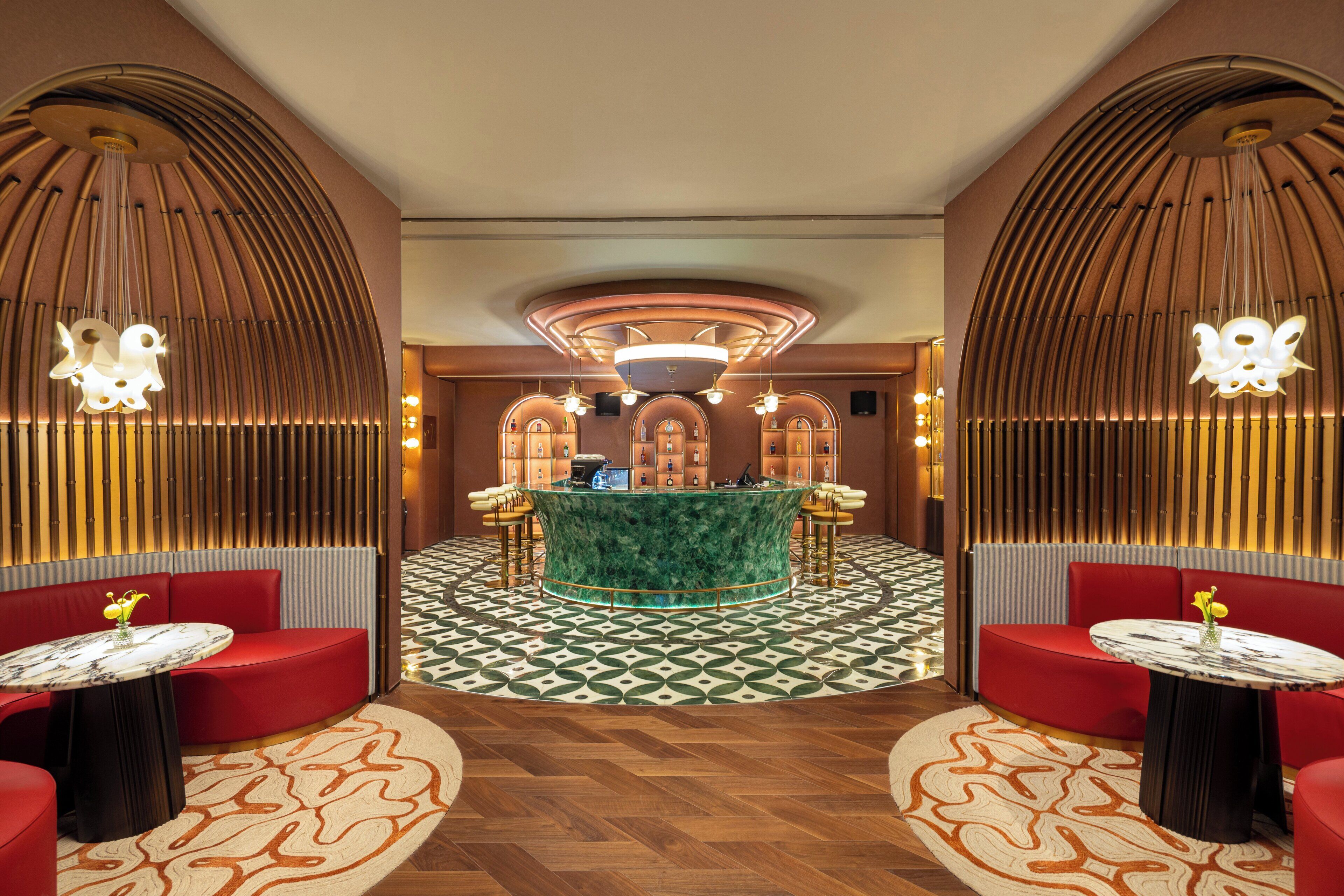 A lobby with a central bar, red seating, patterned flooring, and unique ceiling designs.