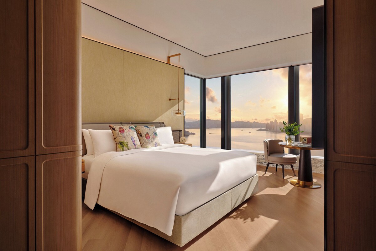 Ein modernes Hotelzimmer mit einem großen Bett, Blick auf die Wüste und einem kleinen Tisch mit einer Pflanze.