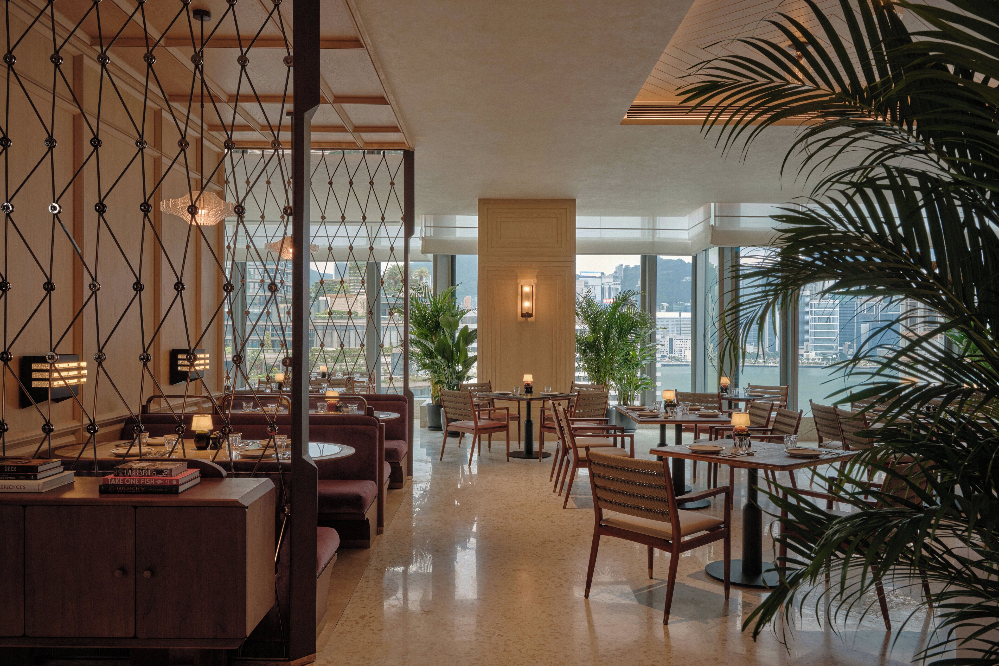 A modern hotel lobby with a high ceiling, large windows, and a mix of seating areas including tables and sofas.