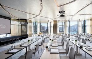 A conference room with a stage, large windows, and a city view. - Kimpton Tsim Sha Tsui Hong Kong by IHG (Kowloon)