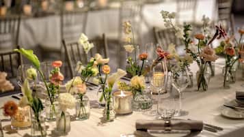 Ein festlich gedeckter Tisch mit Glasvasen, in denen Blumen stehen, und Kerzen.