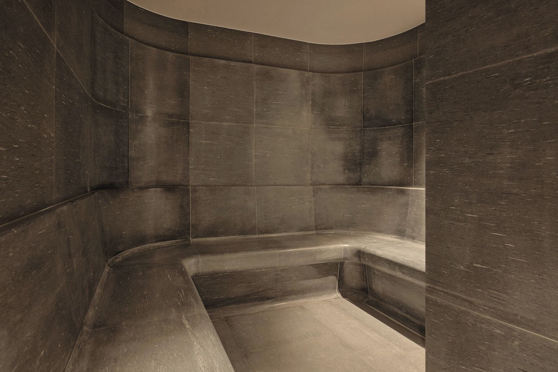 Un baño moderno con tonos oscuros, una zona de ducha curva y un banco integrado.